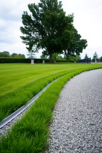Image prompt: A modern garden with clean metal strip edging dividing grass and gravel.