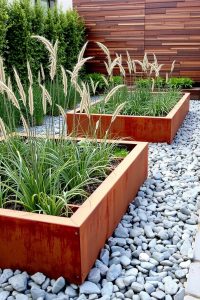 Image Prompt: Raised garden beds made from corten steel with a rusty orange patina, arranged in a modern backyard with rocks and ornamental grasses.